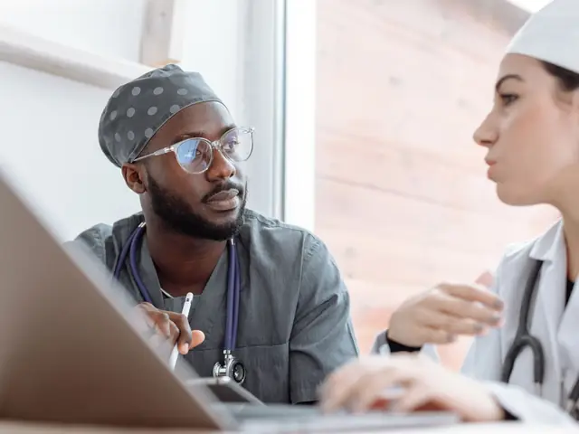 Two health workers discussing notes at a laptop
